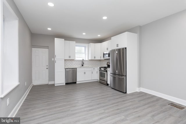 kitchen featuring appliances with stainless steel finishes, white cabinetry, tasteful backsplash, light hardwood / wood-style flooring, and sink