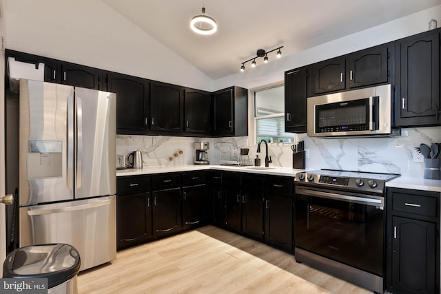 kitchen with light hardwood / wood-style floors, sink, vaulted ceiling, decorative backsplash, and appliances with stainless steel finishes