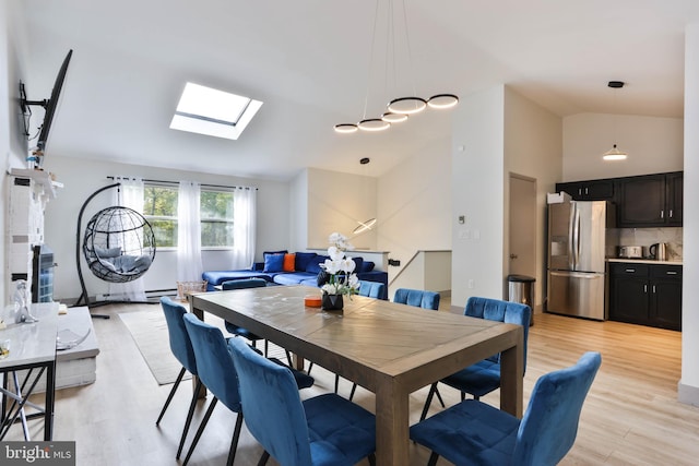 dining room featuring a skylight, light wood-type flooring, and high vaulted ceiling