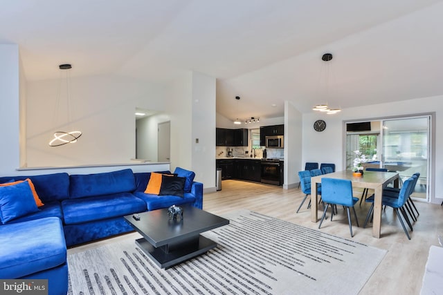 living room with sink, light hardwood / wood-style flooring, and vaulted ceiling