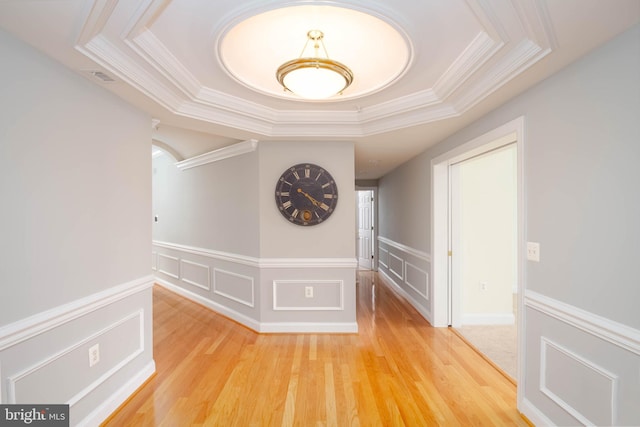 hallway featuring a tray ceiling, light hardwood / wood-style flooring, and ornamental molding