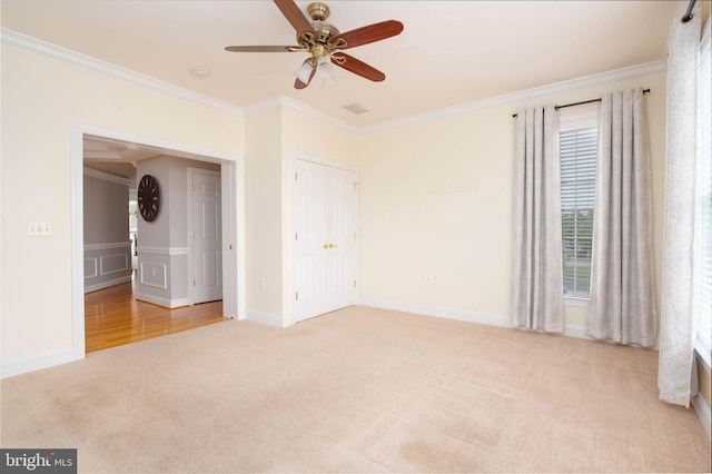 unfurnished bedroom with a closet, light colored carpet, ceiling fan, and crown molding