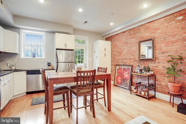 dining room with light hardwood / wood-style floors, brick wall, and sink