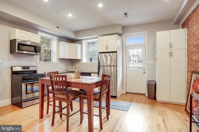 kitchen featuring appliances with stainless steel finishes, white cabinetry, brick wall, light wood-type flooring, and sink