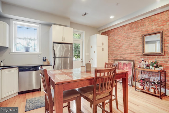 dining space featuring brick wall, sink, and light hardwood / wood-style floors