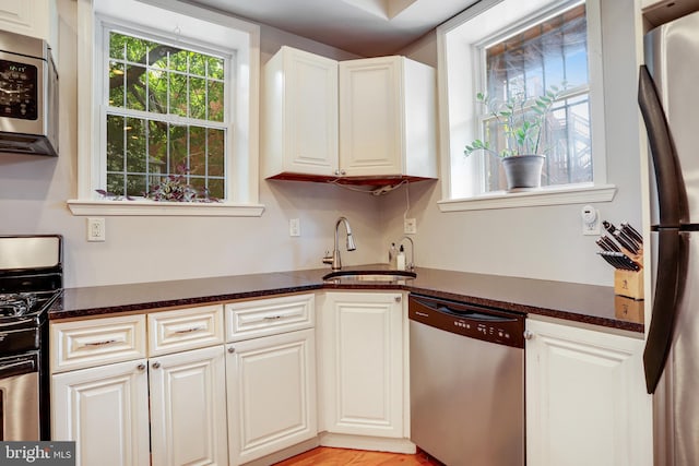 kitchen with light hardwood / wood-style floors, sink, white cabinets, appliances with stainless steel finishes, and dark stone countertops