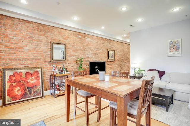 dining area featuring brick wall and light hardwood / wood-style floors