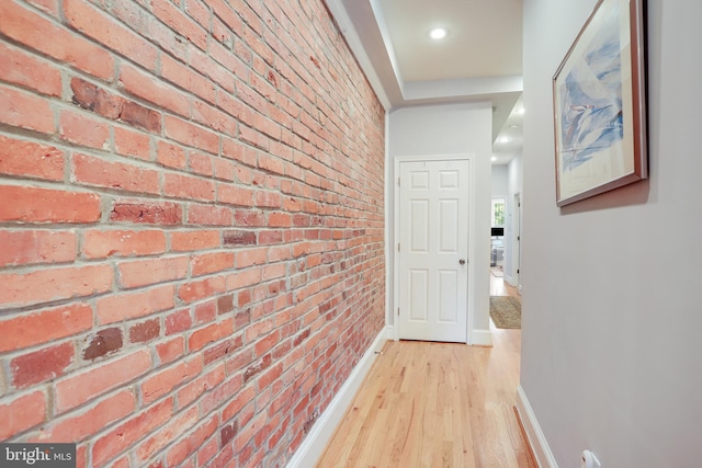 hall with brick wall and light hardwood / wood-style flooring