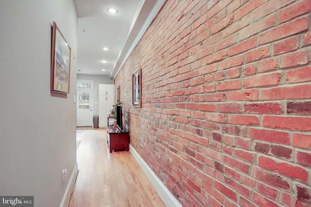 corridor with light hardwood / wood-style floors and brick wall