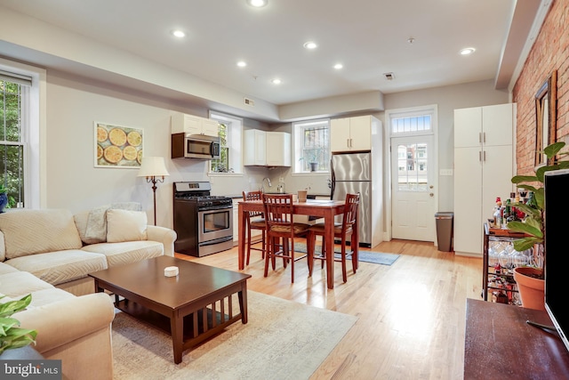 living room featuring brick wall, light hardwood / wood-style flooring, and a healthy amount of sunlight