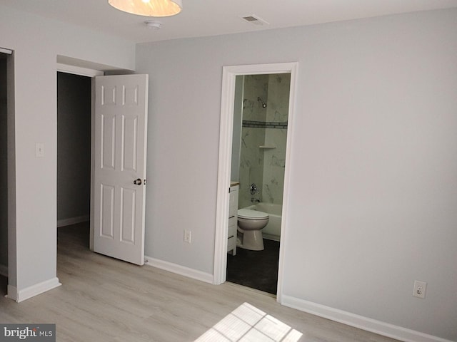 bedroom featuring light hardwood / wood-style flooring, ensuite bath, and a walk in closet