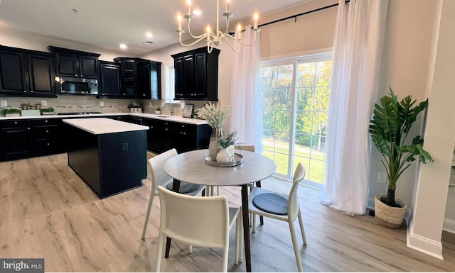 kitchen featuring tasteful backsplash, appliances with stainless steel finishes, a kitchen island, light hardwood / wood-style floors, and decorative light fixtures