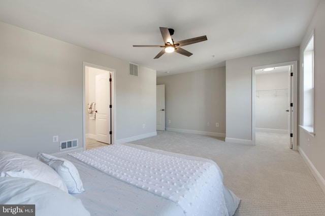 carpeted bedroom featuring a walk in closet, a closet, ensuite bath, and ceiling fan