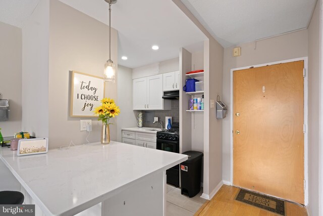 kitchen with white cabinets, kitchen peninsula, black range, decorative light fixtures, and light hardwood / wood-style flooring