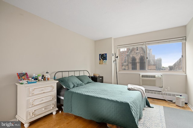 bedroom with light hardwood / wood-style flooring, a baseboard heating unit, and an AC wall unit