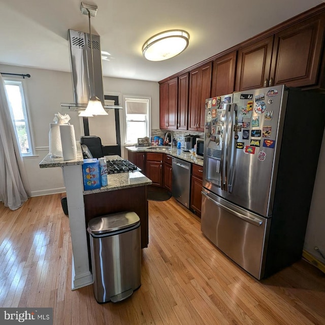 kitchen with light wood-type flooring, sink, ventilation hood, appliances with stainless steel finishes, and light stone countertops