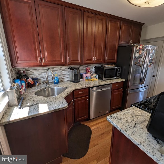 kitchen featuring stainless steel appliances, light stone countertops, light hardwood / wood-style floors, and sink