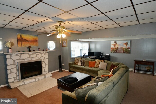 living room with ceiling fan, a stone fireplace, light carpet, and a drop ceiling