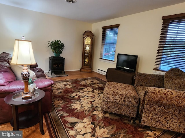 living room featuring a wood stove, plenty of natural light, a baseboard radiator, and hardwood / wood-style flooring