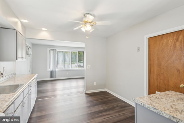 kitchen with light stone counters, dark wood-type flooring, sink, white cabinets, and ceiling fan