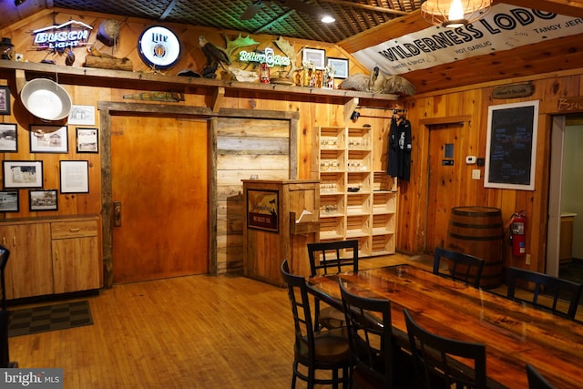 dining area with vaulted ceiling, wood walls, and wood-type flooring