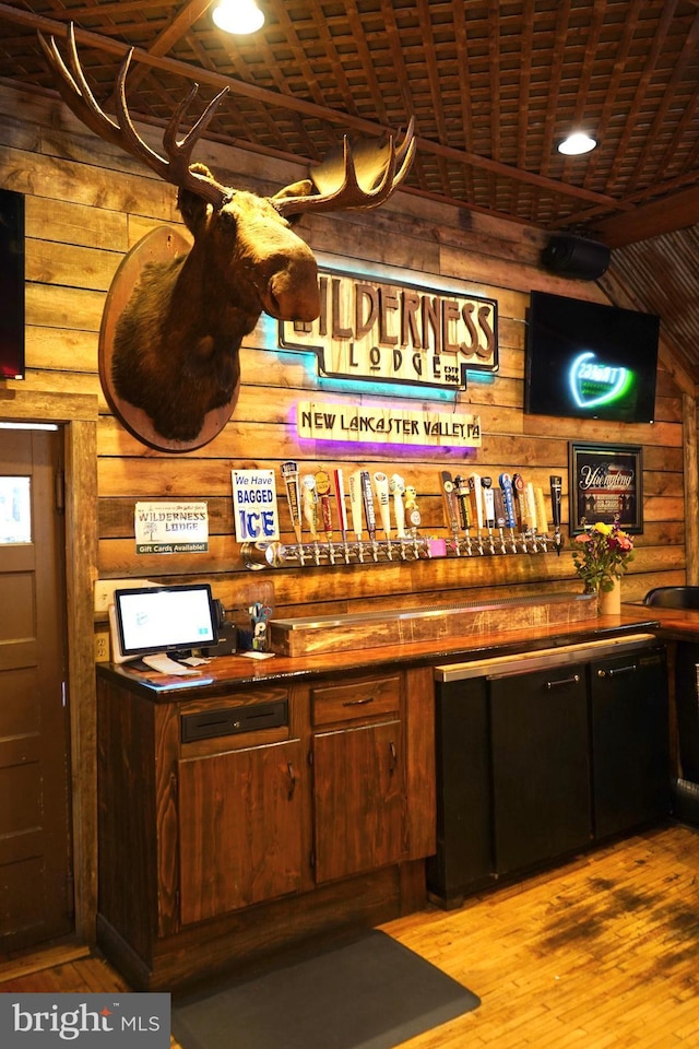 bar with a bar, hardwood / wood-style floors, wooden ceiling, and wood walls