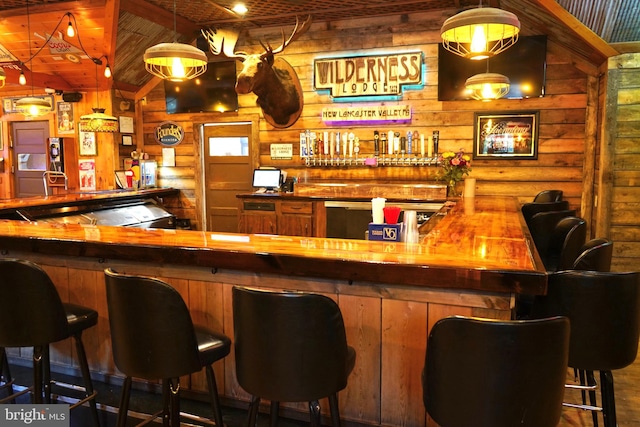 bar with butcher block countertops, pendant lighting, log walls, and vaulted ceiling