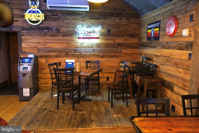 dining space featuring lofted ceiling, wood-type flooring, wooden walls, and an AC wall unit