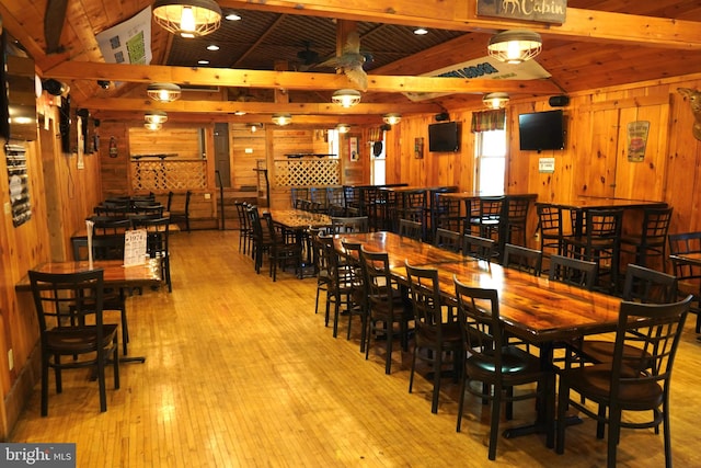 dining room featuring wooden walls, light hardwood / wood-style flooring, ceiling fan, and vaulted ceiling with beams