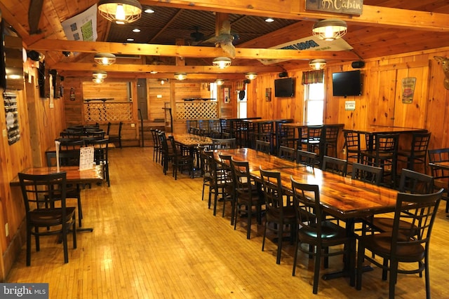 dining room featuring lofted ceiling with beams, wooden walls, and wood-type flooring