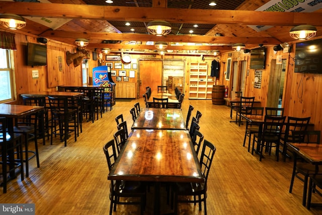 dining room with beamed ceiling, light wood-type flooring, and wooden walls