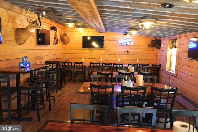 dining area with dark hardwood / wood-style floors, wood walls, and vaulted ceiling with beams