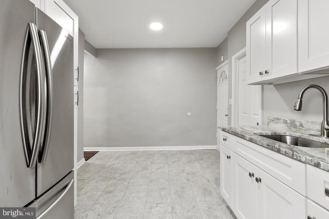 kitchen featuring stainless steel refrigerator, white cabinetry, light stone countertops, and sink