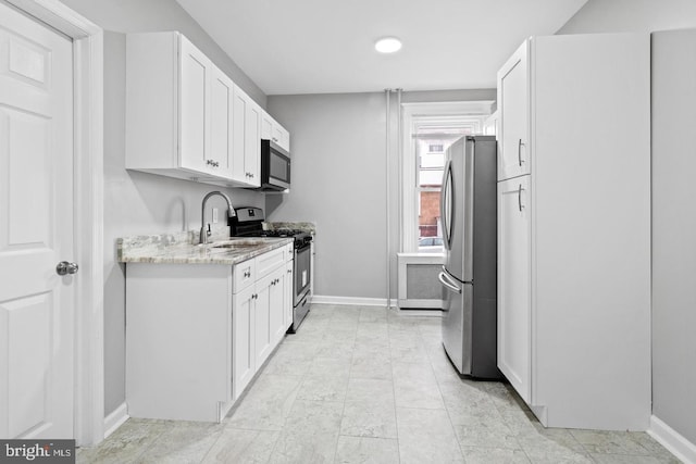 kitchen with light stone counters, white cabinets, appliances with stainless steel finishes, and sink