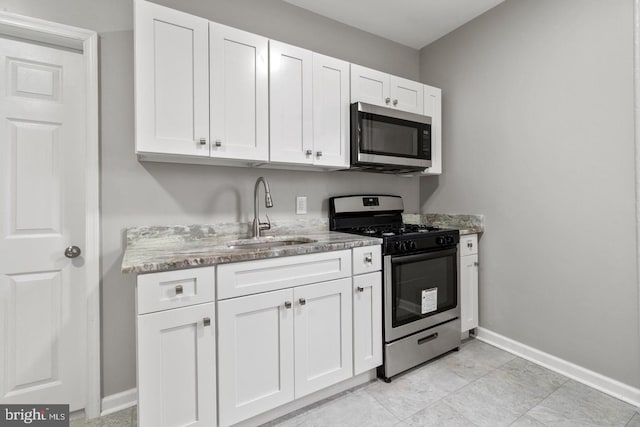 kitchen featuring light stone counters, stainless steel appliances, sink, and white cabinetry