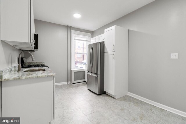 kitchen with white cabinets, stainless steel refrigerator, light stone countertops, and sink