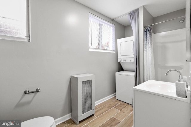 bathroom with wood-type flooring, stacked washing maching and dryer, curtained shower, vanity, and toilet