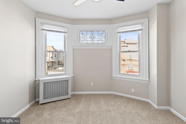 carpeted empty room with a healthy amount of sunlight, radiator, and ceiling fan