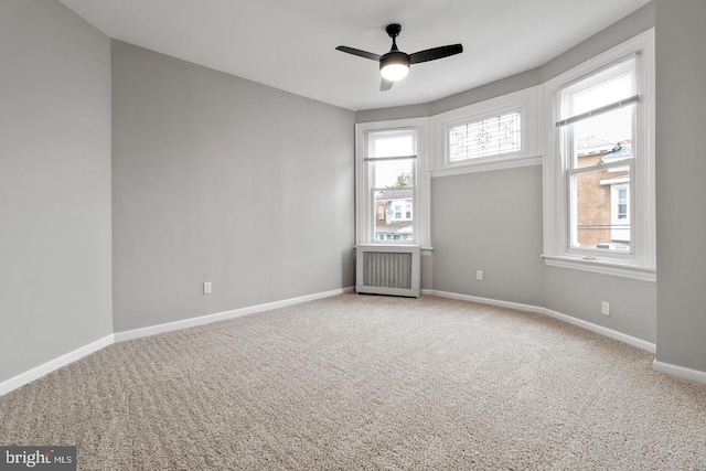 carpeted spare room featuring ceiling fan, radiator, and a healthy amount of sunlight