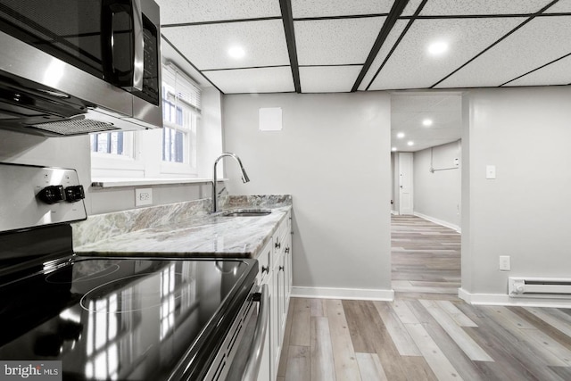 kitchen with light hardwood / wood-style floors, light stone counters, baseboard heating, a drop ceiling, and black electric range