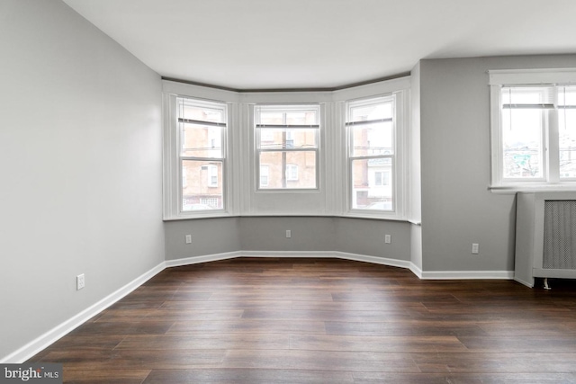 unfurnished room with dark hardwood / wood-style floors, radiator heating unit, and a wealth of natural light