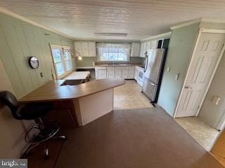 kitchen with white cabinetry, kitchen peninsula, stainless steel fridge, a breakfast bar, and ornamental molding