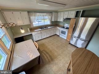 kitchen featuring white cabinets, stainless steel fridge, white range, and sink