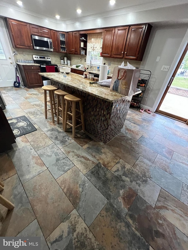 kitchen featuring crown molding, backsplash, kitchen peninsula, light stone countertops, and a breakfast bar