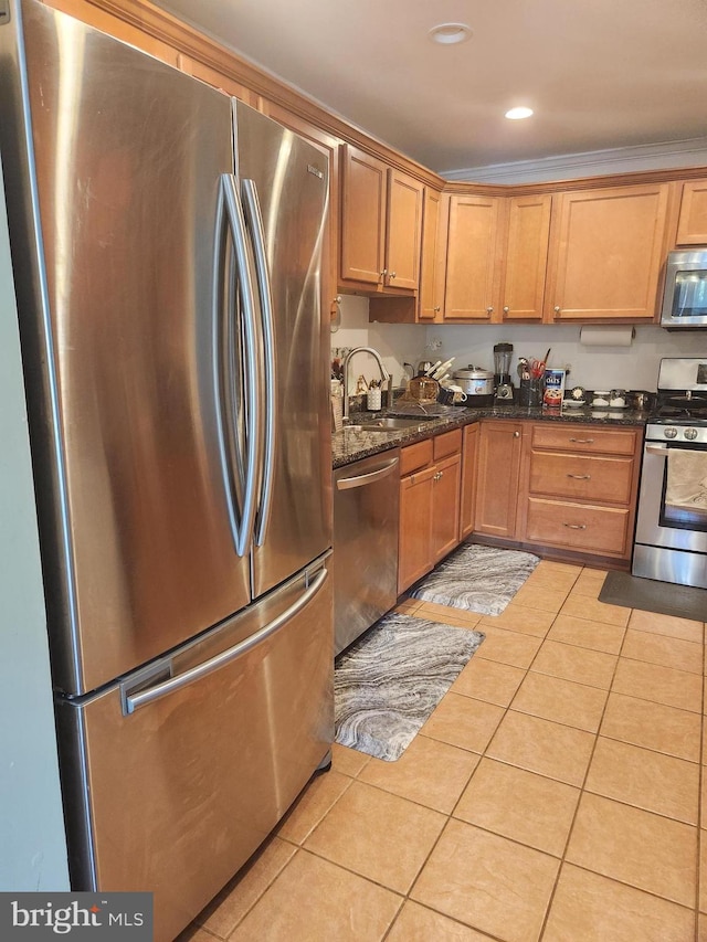 kitchen featuring light tile patterned flooring, ornamental molding, sink, stainless steel appliances, and dark stone counters