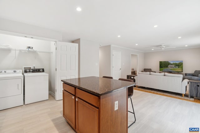 kitchen with dark stone countertops, independent washer and dryer, light hardwood / wood-style floors, a center island, and ceiling fan