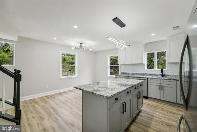 kitchen featuring pendant lighting, gray cabinets, a center island, light wood-type flooring, and decorative backsplash