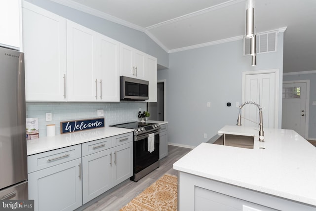 kitchen featuring vaulted ceiling, light wood-type flooring, decorative light fixtures, appliances with stainless steel finishes, and sink