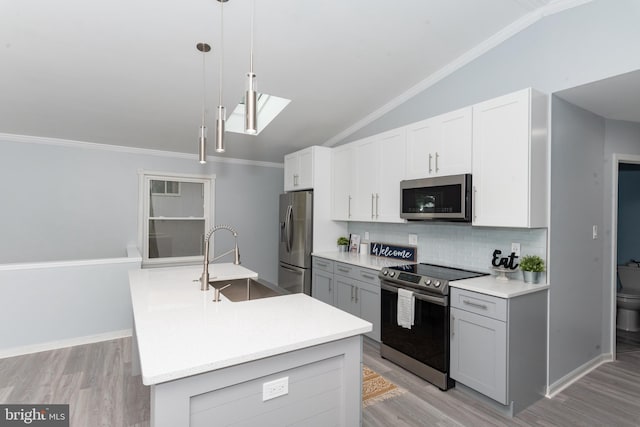 kitchen with lofted ceiling with skylight, light hardwood / wood-style flooring, appliances with stainless steel finishes, hanging light fixtures, and sink