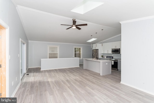 kitchen featuring vaulted ceiling with skylight, a kitchen island with sink, stainless steel appliances, ceiling fan, and white cabinets